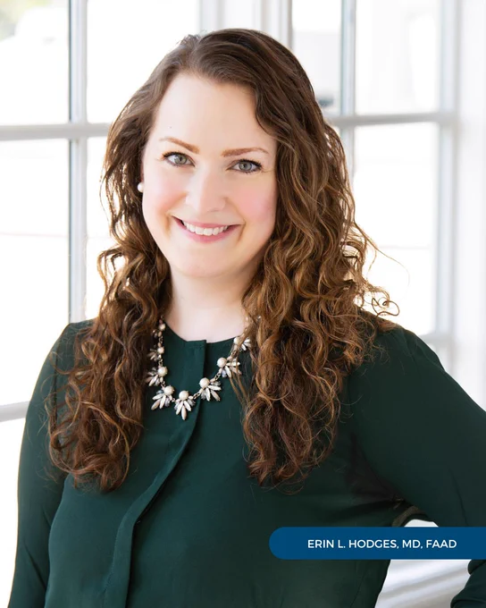 Dr. Erin Hodges of Tryon Medical Partners smiles in a professional portrait wearing an emerald green sweater standing in front of a paned glass window backdrop
