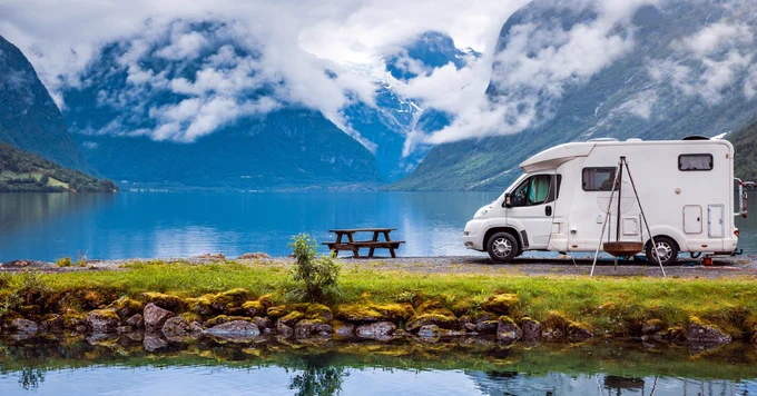 An RV is parked beside a lake on a cloudy morning.