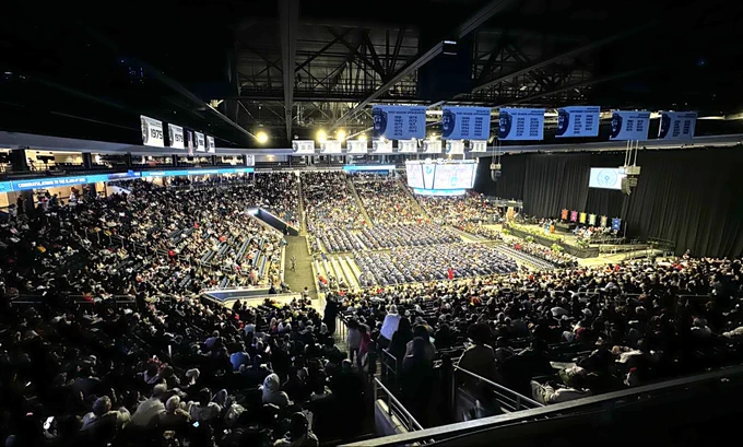 Arena full of seated audience members and graduates during commencement ceremony.