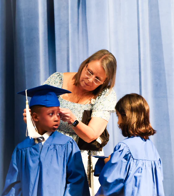 ELC 1 director, Jennifer, helping one of her PreK students put his cap on for the celebration.