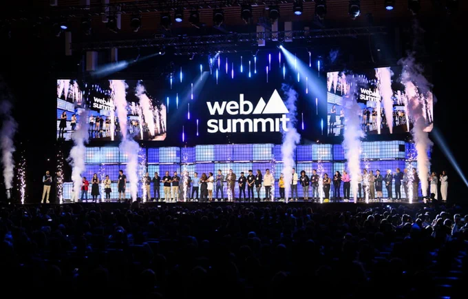  A large stage with purple lights and a group of people standing in front of a large Web Summit logo.