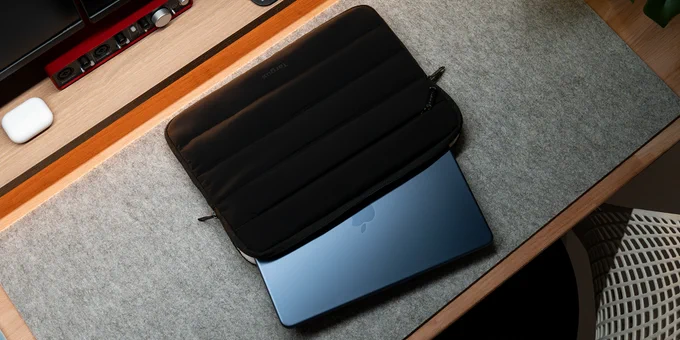 Slim black laptop sleeve partially open with a sleek blue laptop inside on a gray felt surface.