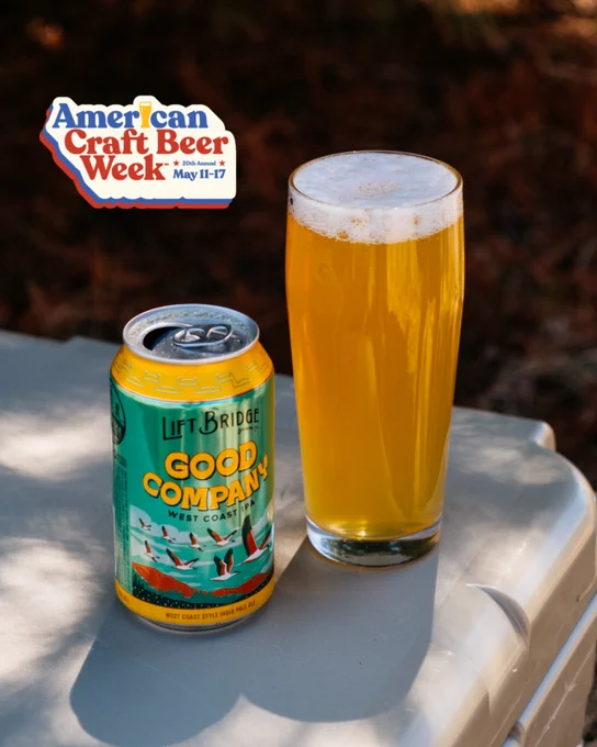 A can of Lift Bridge Good Company West Coast IPA next to a glass of beer on a table outdoors. The event badge for American Craft Beer Week is visible.