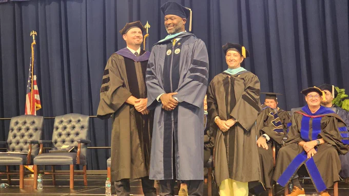 A male graduate smiles for a photo after his doctoral hooding.
