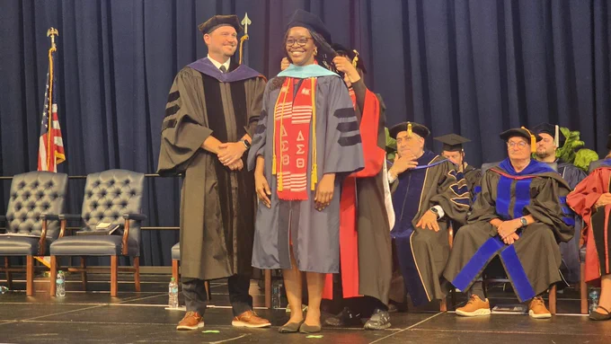 A female graduate smiles for a photo after her doctoral hooding.