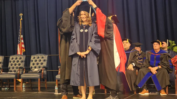 A female graduate smiles as she is hooded for earning her doctoral degree.