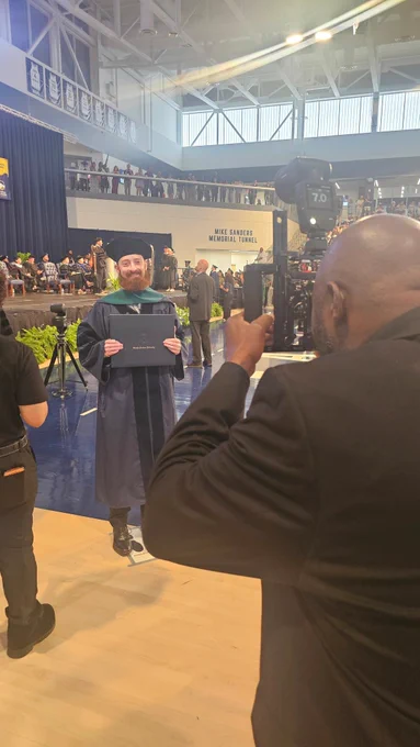 A male doctoral graduate with a beard poses for a photo with his degree cover.