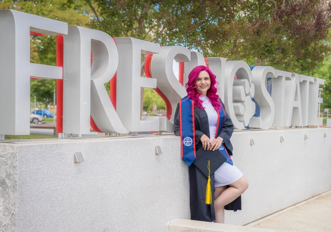 Felicia in grad regalia poses for a photo in front of Fresno State sign.