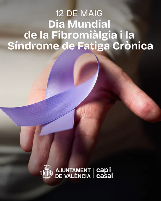 Cartell del Dia Mundial de la Fibromiàlgia i la Síndrome de Fatiga Crònica. Sobre una fotografia desenfocada en tons càlids, apareix una mà subjectant un llaç morat, símbol de suport i conscienciació. A la part superior, en lletres blanques grans, es llig: “12 DE MAIG. Dia Mundial de la Fibromiàlgia i la Síndrome de Fatiga Crònica”. A la part inferior apareix el logotip de l’Ajuntament de València amb el lema “cap i casal”, també en blanc.