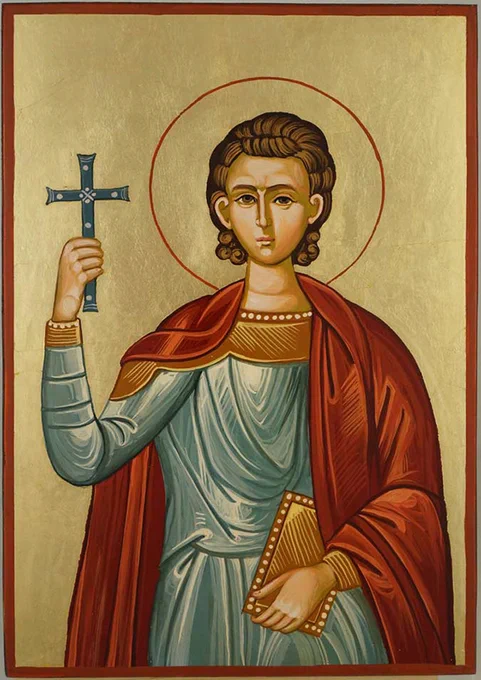 Byzantine-style painted icon of Saint Pancras, depicted as a young man with curly brown hair and a gold halo. He wears a blue-grey robe and red cloak, holds a decorated cross aloft in his right hand, and carries a gold-covered book in his left. The background is gold leaf.