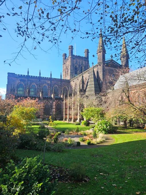 Red sandstone Chester Cathedral viewed from the side. Blue sky, garden and some foliage to the front