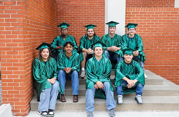 Eight students in caps and gowns.