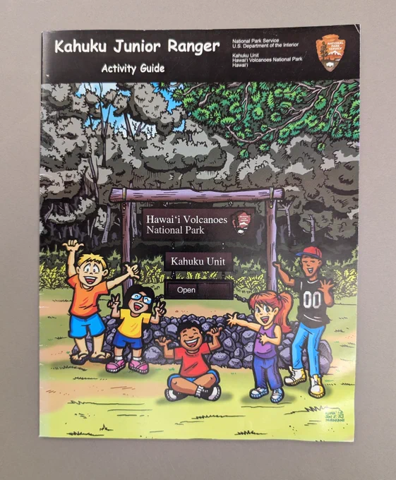 Illustrated cover of Kahuku Junior Ranger Activity Guide featuring five children happily posing in front of Hawai'i Volcanoes National Park sign. Guidebook is in the Interior Museum's collection, Interior Museum, INTR 07931, gift of Ryan Deacy and the staff of the Kahuku Unit of Hawaii Volcanoes National Park.