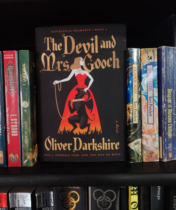 my bookshelf, with a copy of The Devil and Mrs Gooch, feat. the eponymous Gwendolyn Gooch who has the goatlike Devil in a leash and collar by her feet