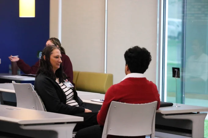 Two people engaged in conversation while seated at desks.