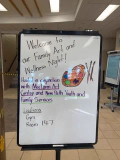 Whiteboard announcing Family Art and Wellness Night with a colorful artist palette drawing and event details at MacLaren Art Centre and New Path Youth and Family Services.