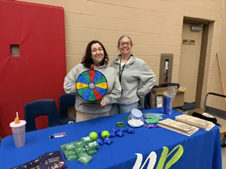 Two people standing behind a New Path branded table with SWAG and promotional items on it. 