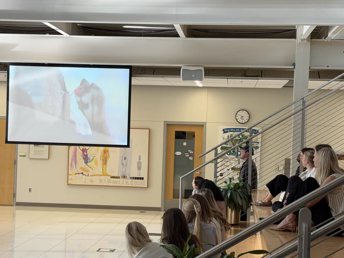 People sitting in an atrium gazing at a large projected screen displaying an artistic image.