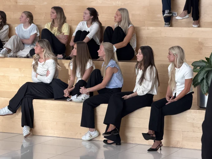 A group of young women in casual business attire sitting on steps in a lobby.
