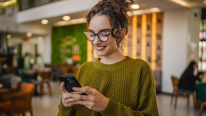 Image of a person at home or in a café signing up for auto debit on their phone with headline: “Auto Debit: Save Time and Money With Simple Sign-Up” 