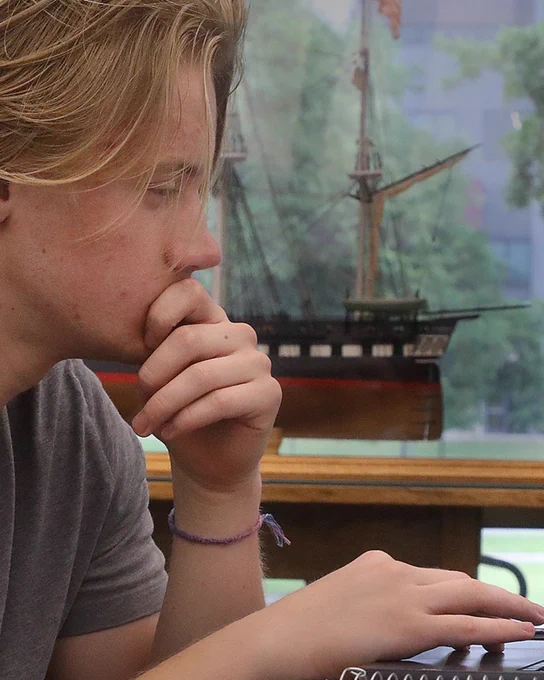 Student studying in a library, model boat in the background. 