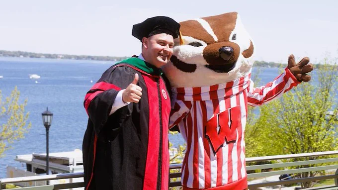 Man in academic regalia with bucky the badger mascot