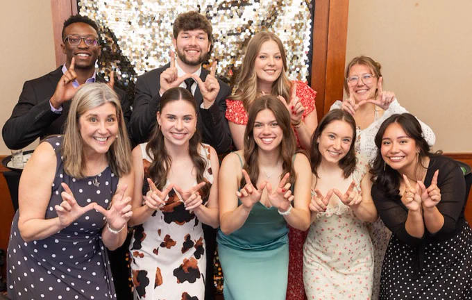 Nine men and women smiling and making W symbol with their fingers