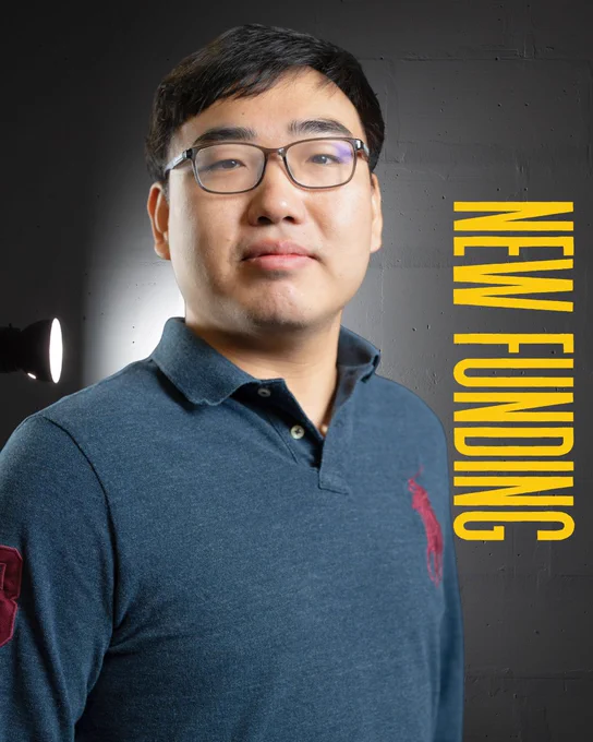 Portrait of Bo Xiao standing in front of a dark gray textured background. He is wearing glasses and a dark blue collared shirt, facing the camera with a neutral expression. The words “NEW FUNDING” appear vertically in gold lettering along the right side of the image.