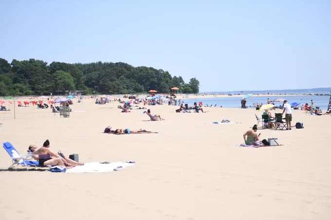 Orchard Beach filled with patrons and umbrellas near water and trees. 
