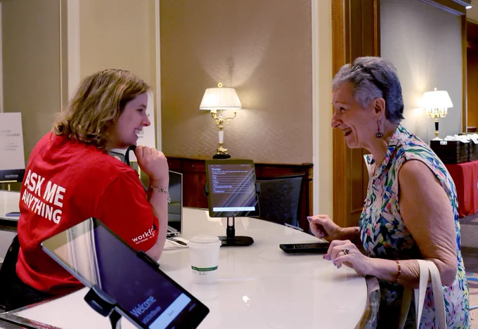 Two individuals smiling at registration desk in front of tablets