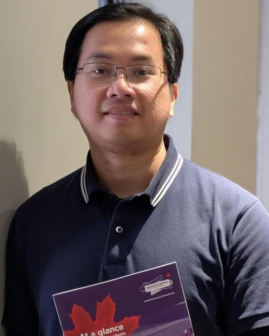 Student council member, Xuan Vinh Vu, wearing a grey polo shirt and holding a book. 