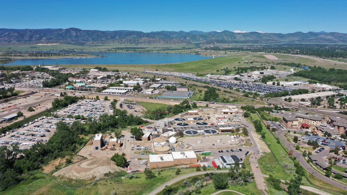 Aerial view of a wastewater treatment facility with the Colorado mountains and a small reservoir in the distance.