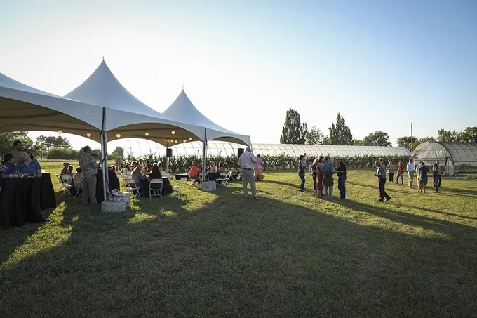 People gathered under party tents with a hoop house in the background during a previous Farmers for Tomorrow Fund benefit.
