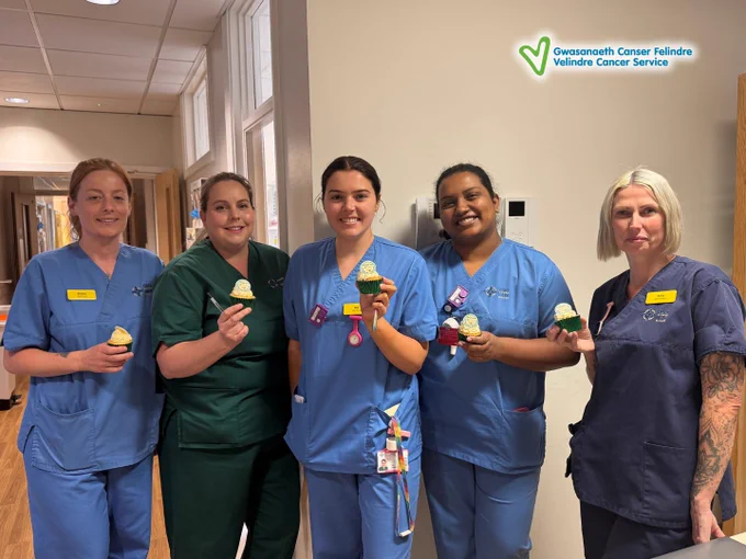 Five healthcare workers in scrubs holding cupcakes, standing in a hospital corridor.