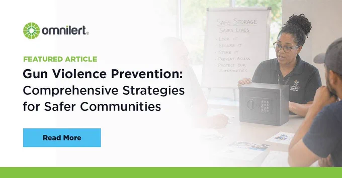 A graphic. The left half is white and fades into an image of a safe gun storage training session on the right half. A green bar lines the bottom. On the white half, in small green text it says "Featured Article," and below it, in larger black font "Gun Violence Prevention: Comprehensive Strategies for Safer Communities." Above the text is the Omnilert logo, and below it is a non-clickable button that says "Read More."
