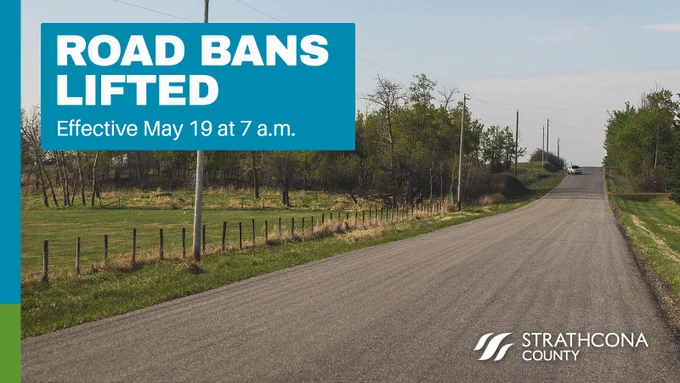 Rural road stretching into the distance with announcement that road bans are lifted starting May 19 at 7 a.m.