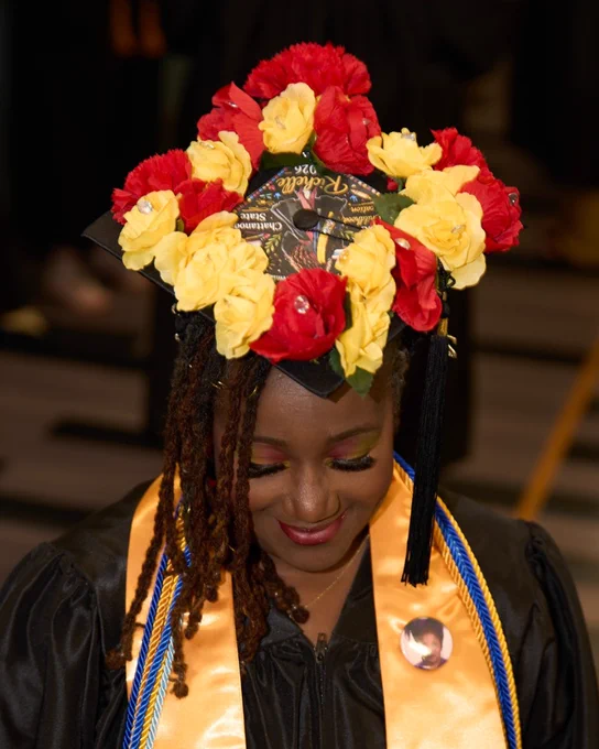 Graduation cap decorated with red and yellow flowers worn by a graduate in black gown and gold stole at Chattanooga State graduation.