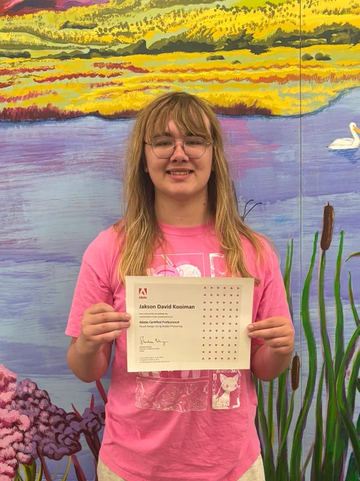 Image of a student holding an Adobe certificate for Photoshop, standing in front of a colorful mural