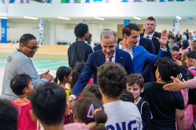 Prime Minister Mark Carney and the Secretary of State for Sport, Adam van Koeverden, are shaking hands and high-fiving children at the MLSE Launchpad youth recreation complex in Toronto.   