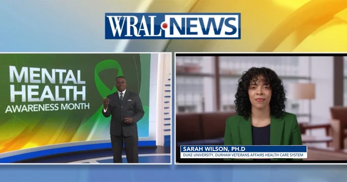 WRAL News broadcast featuring a segment on Mental Health Awareness Month. A person stands in front of a graphic with text, and another is shown on a video call. The text on screen reads, 'Sarah Wilson, Ph.D., Duke University, Durham Veterans Affairs Health Care System.'"