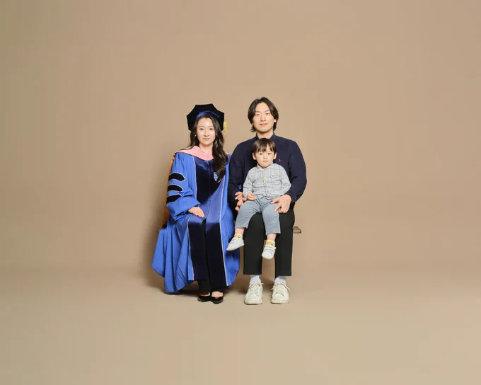 Mideum Hong is pictured with his wife and child, photographed against a beige photo studio background.