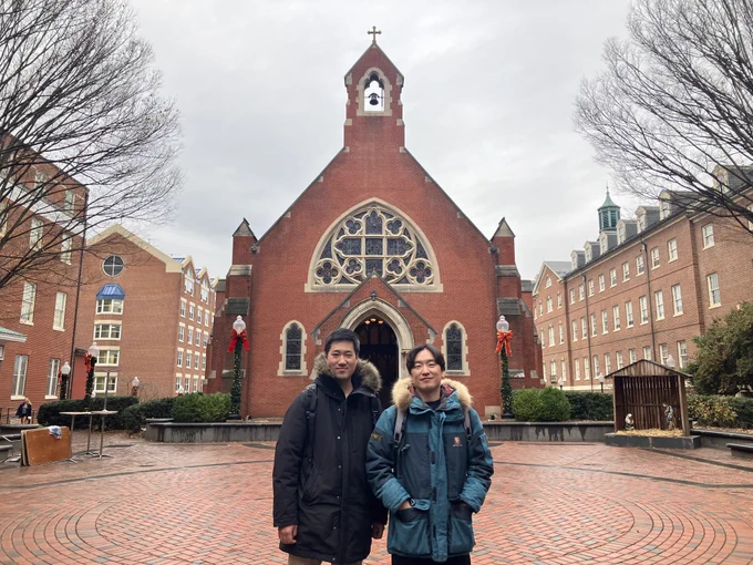 Mideum Hong, right, stands next to Haweon Lee in front of Dahlgren Chapel. Both men are wearing winter coats and the chapel is decorated for Christmas.