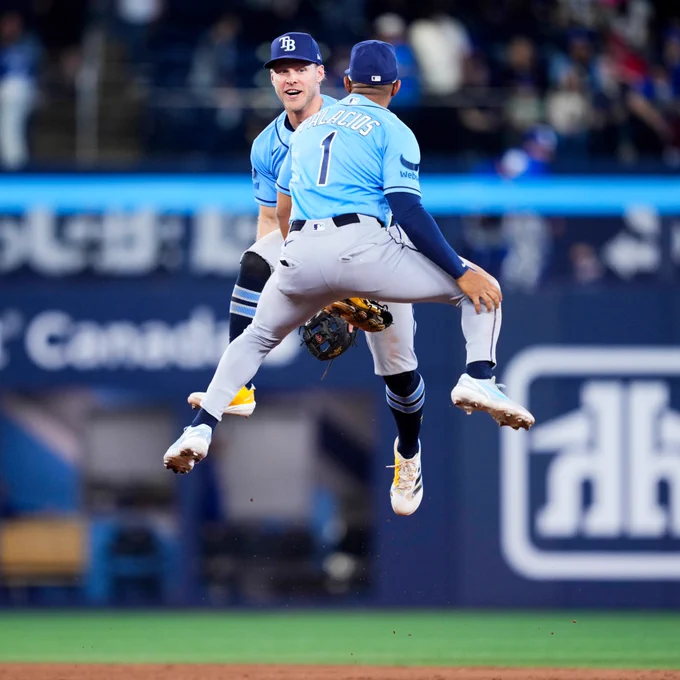 Taylor Walls and Richie Palacios celebrate by jumping high after the Rays win Monday night in Toronto. They wear light blue Rays uniforms.