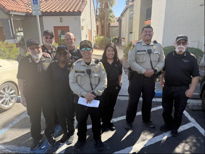 Group of chaplains and LVMPD officers standing together outside residential buildings on a sunny day.