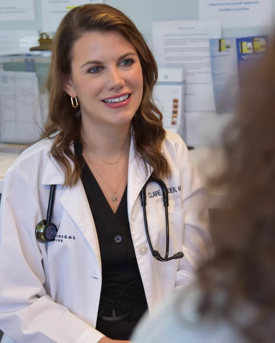 Dr. Claire Wilder of Tryon Medical Partners sits and smiles in an exam room while speaking to a patient.