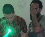 In an image from court documents, Westyn Lantigua can be observed at the left making a Trinitario gang sign and holding a firearm with a green laser that he is pointing at the camera.