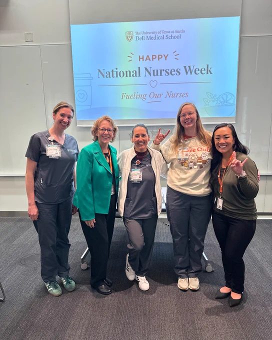 Group of five individuals standing and smiling in front of a presentation screen that reads, "University of Texas at Austin Dell Medical School - Happy National Nurses Week - Fueling Our Nurses."