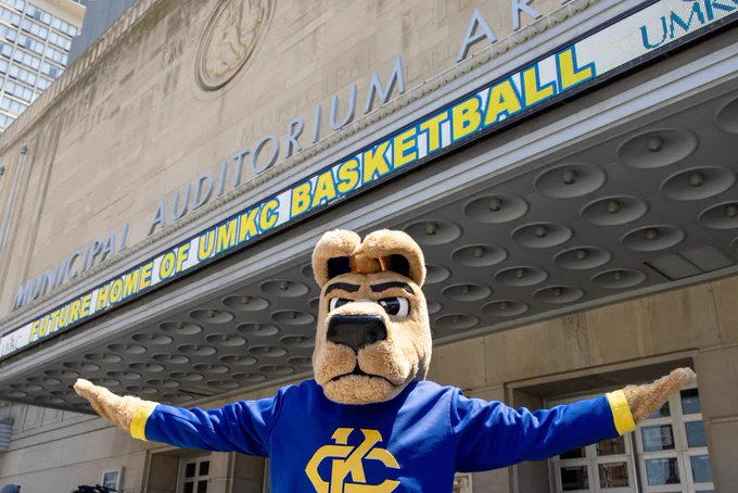 KC Roo mascot poses for a photo in front of Municipal Auditorium. The marquee reads "Future Home of UMKC Basketball"