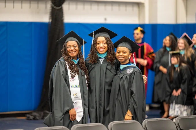 Three smiling graduates in black gowns and caps.