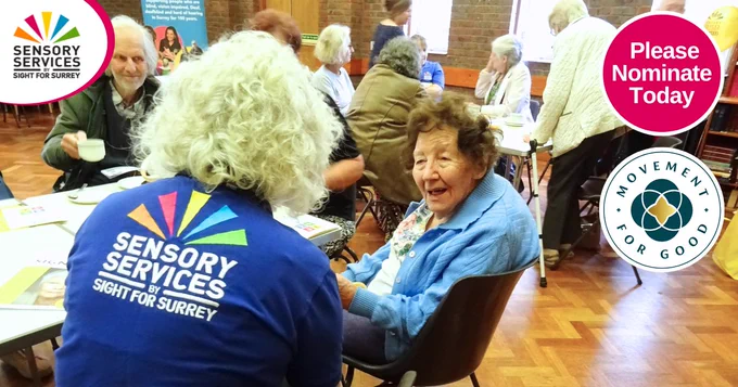 A group of senior people chatting together at a coffee morning in a village hall. A member of our team, wearing blue branded polo shirt, sits chatting with a lady at a table. Top right bubble reads: "Please Nominate Today". Below is a Movement for Good logo. 